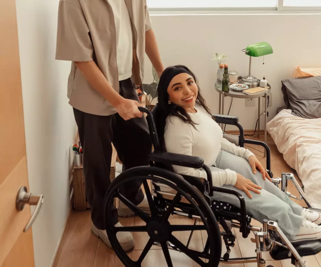 Disabled woman in wheelchair smiling at camera with carer standing behind her